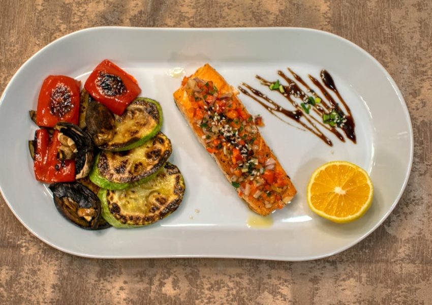 Gourmet grilled salmon served with roasted vegetables and lemon slice on a white plate.