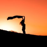 A woman holding fabric gracefully in silhouette against a vibrant sunset in Türkiye.