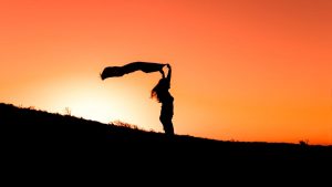 A woman holding fabric gracefully in silhouette against a vibrant sunset in Türkiye.